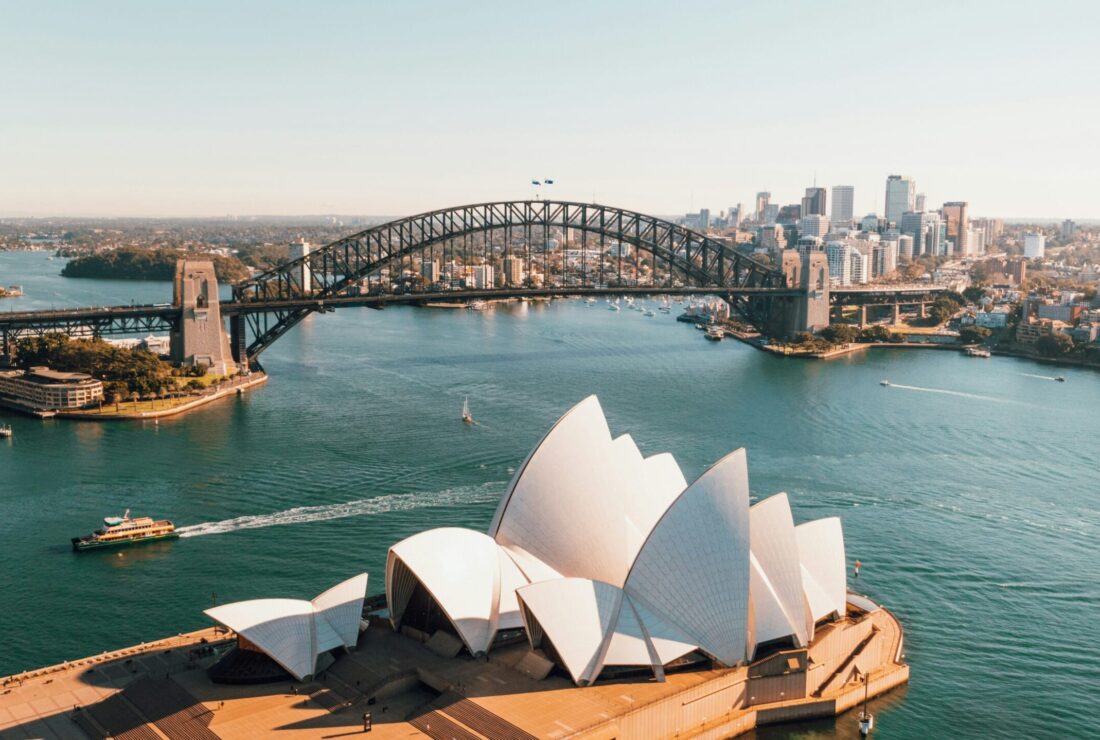 Aerial view of the Sydney Opera House and the Sydney Harbour Bridge over the blue water on a clear day.